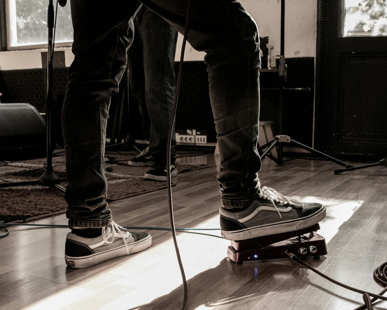 Nahaufnahme eines Musikers mit Sneakern am Effektpedal im Proberaum.