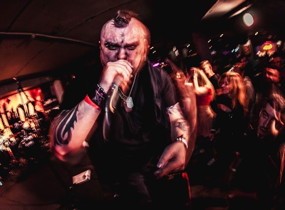 Tätowierter Metal-Sänger singt ins Mikrofon vor tanzendem Publikum
