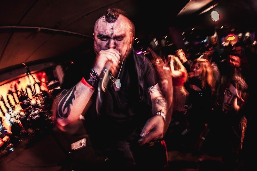 Tätowierter Metal-Sänger singt ins Mikrofon vor tanzendem Publikum