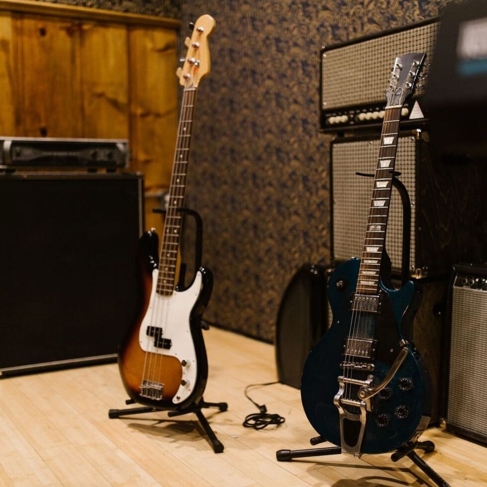 E-Gitarre und Bass vor mehreren Vintage-Verstärkerboxen im Proberaum