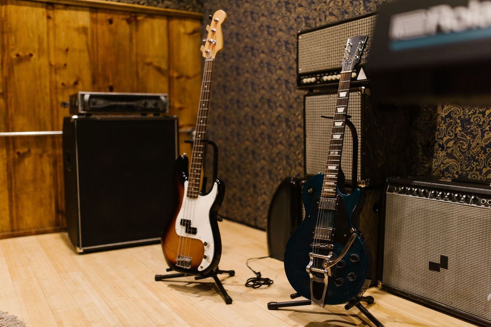 E-Gitarre und Bass vor mehreren Vintage-Verstärkerboxen im Proberaum